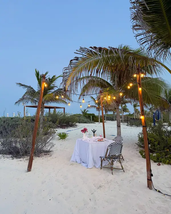A dinner table set on the beach under string lights at dusk