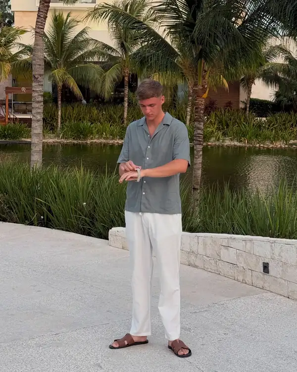 Leon checking his watch on a path lined with palm trees